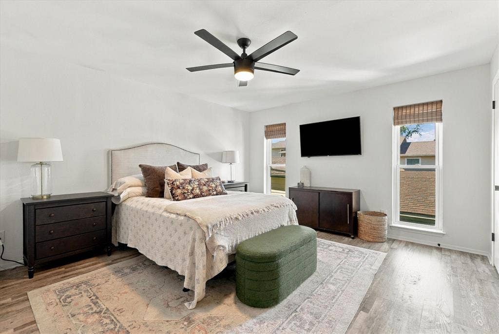1955 Shorewood Drive, Grapevine, TX 76051 Room featuring wood-finish flooring, a matte black multi-blade ceiling fan with integrated lighting, and two windows with installed window shades
