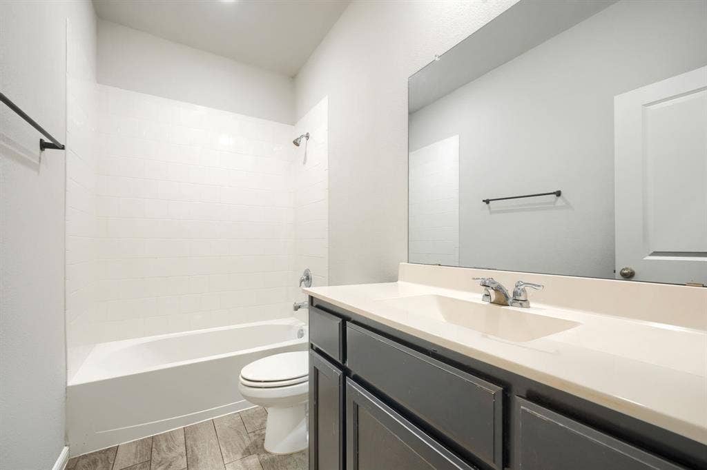 Bathroom featuring a vanity with a solid-surface countertop, an integrated sink basin, wood-finish flooring, a full-width vanity mirror, and a tub-shower combination with tile surround
