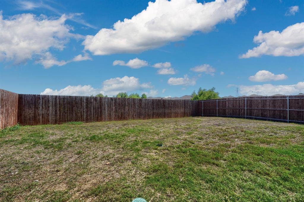 Expansive backyard area featuring a grass lawn enclosed by full-height wood fencing