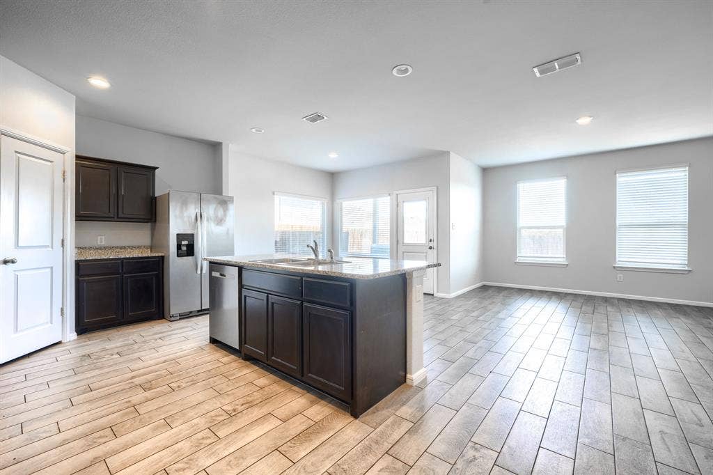 Kitchen featuring dark cabinetry, stone-finish countertops, stainless steel appliances, a center island with a built-in dishwasher, and wood-finish tile flooring