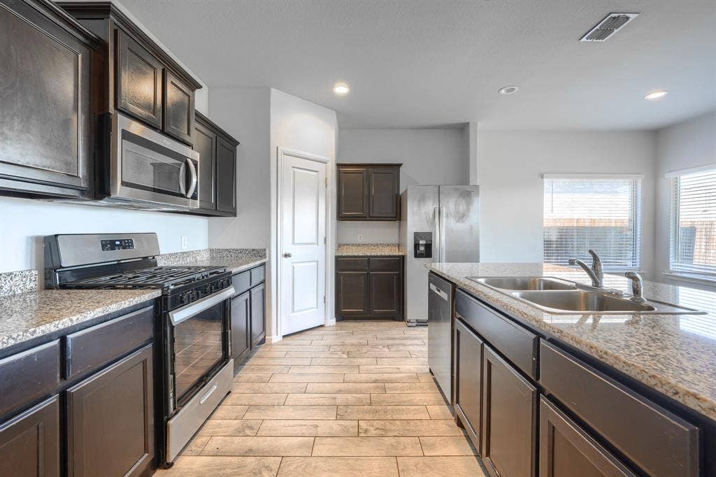 Kitchen featuring dark wood cabinetry, stone-surface countertops, tile flooring, stainless steel appliances, and a dual-basin sink