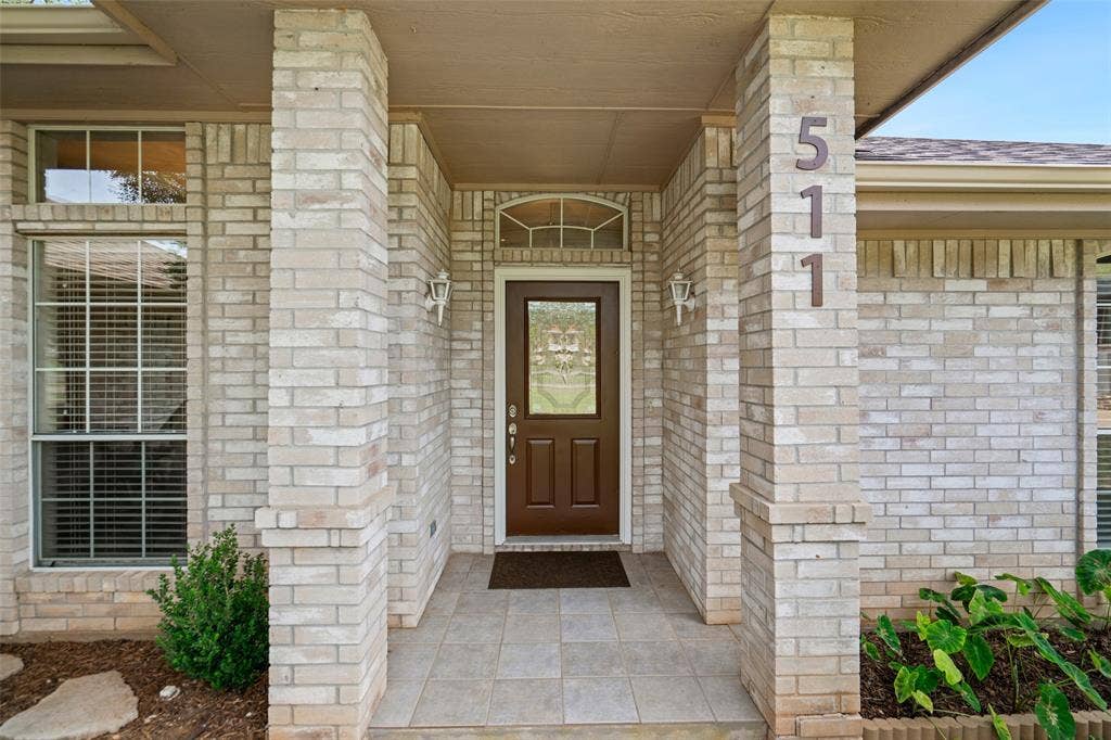 511 Casas Del Norte Court, Granbury, TX 76049 Covered entryway featuring light brick columns, a decorative arch-top transom window, tile flooring, and wall-mounted carriage lights
