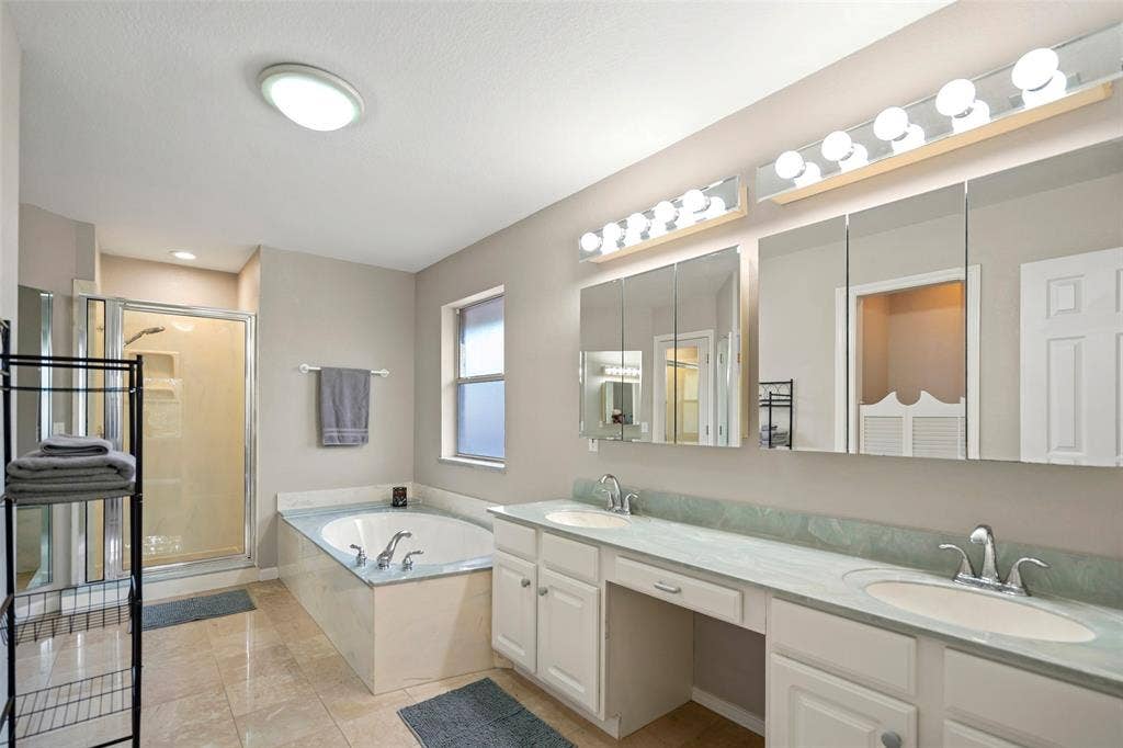 511 Casas Del Norte Court, Granbury, TX 76049 Dual-sinks vanity with countertop seating, garden tub, walk-in glass-enclosed shower, triple-panel mirrored medicine cabinet, tile flooring