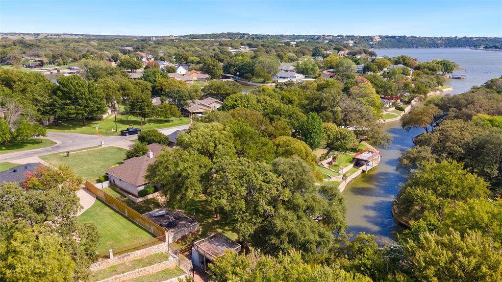 511 Casas Del Norte Court, Granbury, TX 76049 Waterfront property featuring a private boat dock, terraced stone retaining walls, mature trees, and expansive grassy grounds
