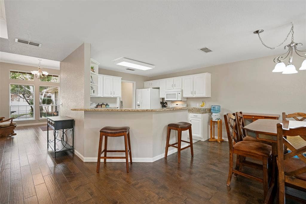 511 Casas Del Norte Court, Granbury, TX 76049 Kitchen featuring white cabinetry, a granite breakfast bar, wood-finish flooring, and a multi-light chandelier in the breakfast nook