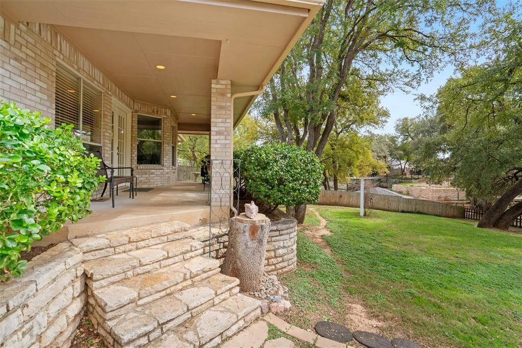511 Casas Del Norte Court, Granbury, TX 76049 Covered porch featuring brick exterior siding, recessed lighting, and stone steps, paired with a landscaped backyard containing mature trees and stone retaining walls