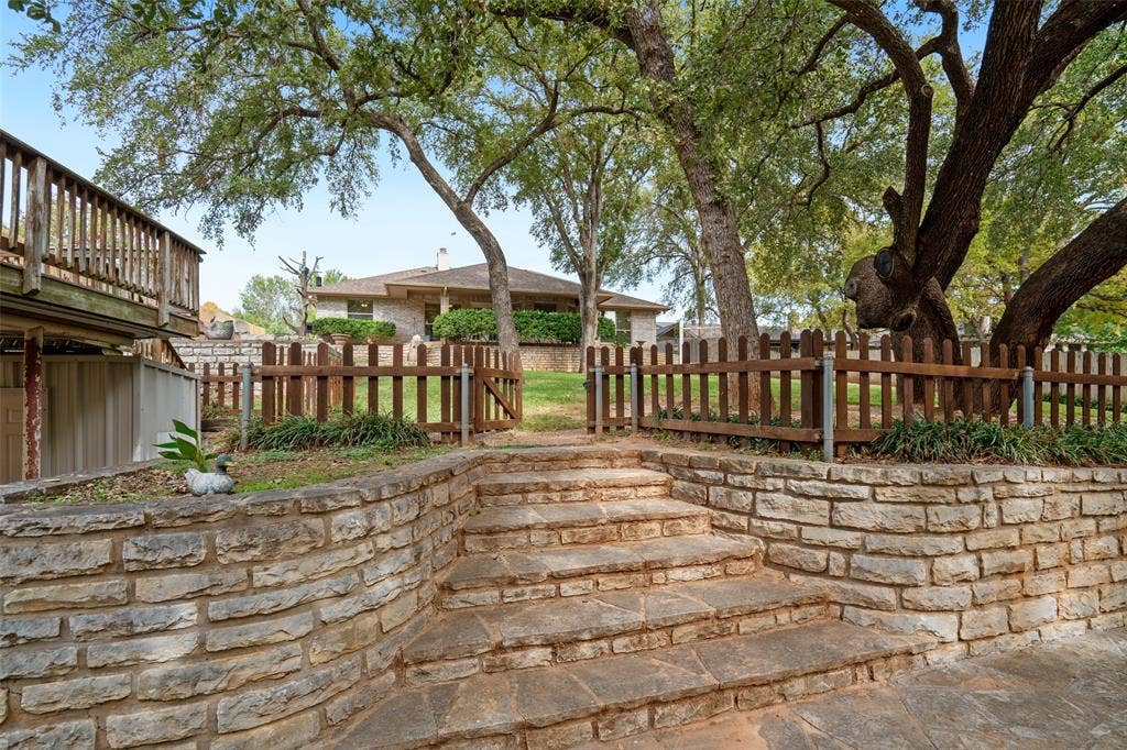 511 Casas Del Norte Court, Granbury, TX 76049 Tiered stone retaining walls, natural flagstone stairs, wood-slat fencing, and mature canopy trees
