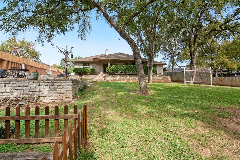 511 Casas Del Norte Court, Granbury, TX 76049 Expansive backyard featuring a tiered stone retaining wall, mature shade trees, perimeter wood fencing, and a manicured lawn