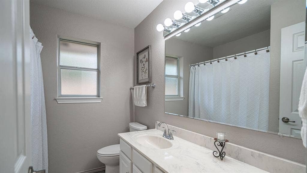 511 Casas Del Norte Court, Granbury, TX 76049 Bathroom featuring a vanity with solid surface countertop and sink, a vanity mirror, integrated multi-bulb vanity lighting, and a window with frosted glass