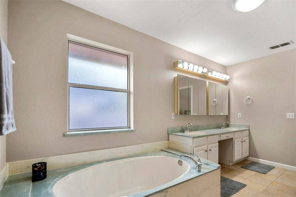 511 Casas Del Norte Court, Granbury, TX 76049 Bathroom featuring a garden tub with solid-surface surround, dual-sink vanity with built-in cabinetry, tri-fold mirrored medicine cabinet, multi-bulb vanity lighting, and ceramic tile flooring