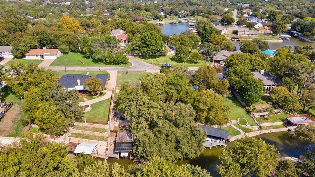 511 Casas Del Norte Court, Granbury, TX 76049 Aerial perspective of a waterfront property featuring a multi-tiered stone retaining wall, private boat slip, mature trees, and direct access to the waterway
