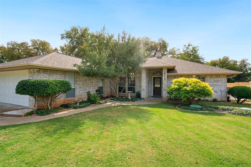 511 Casas Del Norte Court, Granbury, TX 76049 Single-story masonry exterior featuring a hip roof, two-car garage, recessed entryway, and manicured landscaping