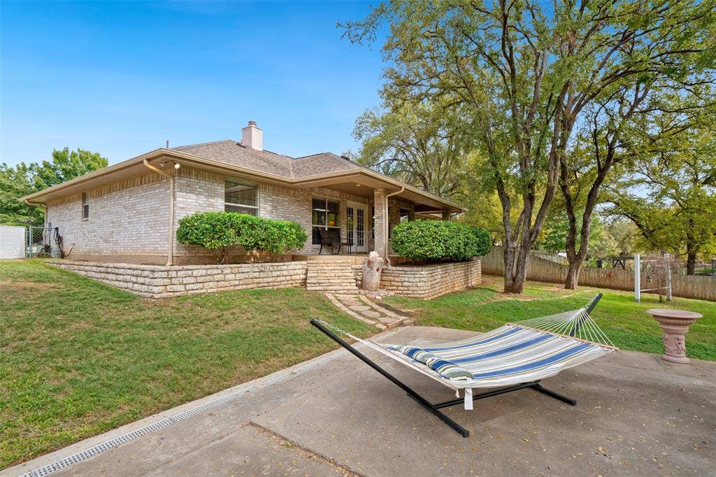 511 Casas Del Norte Court, Granbury, TX 76049 Exterior brick façade featuring a covered patio, stacked-stone retaining walls, stone-tread steps, and mature tree-lined landscaping
