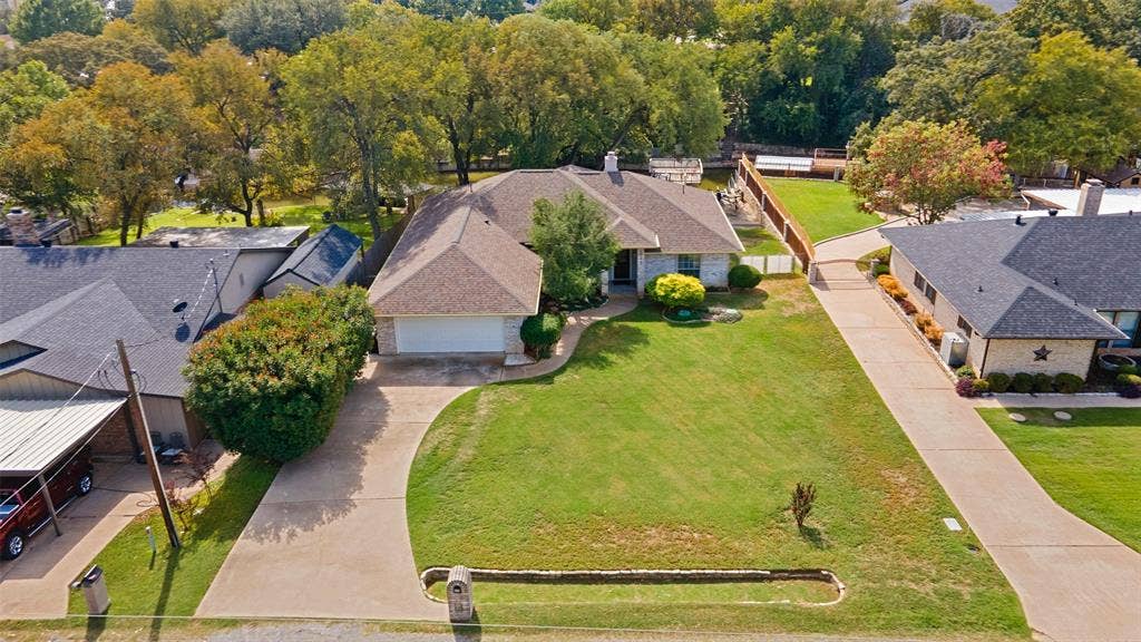 511 Casas Del Norte Court, Granbury, TX 76049 Single-story residence featuring a brick and stone facade, multi-gable roofline, two-car garage, and expansive front lawn with a concrete driveway