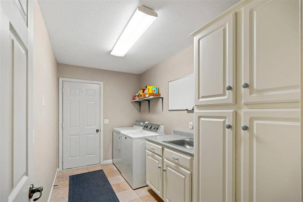 511 Casas Del Norte Court, Granbury, TX 76049 Utility area featuring shaker-style cabinetry-pantry, an integrated stainless steel sink with solid-surface countertop, tile flooring, and wall-mounted shelving
