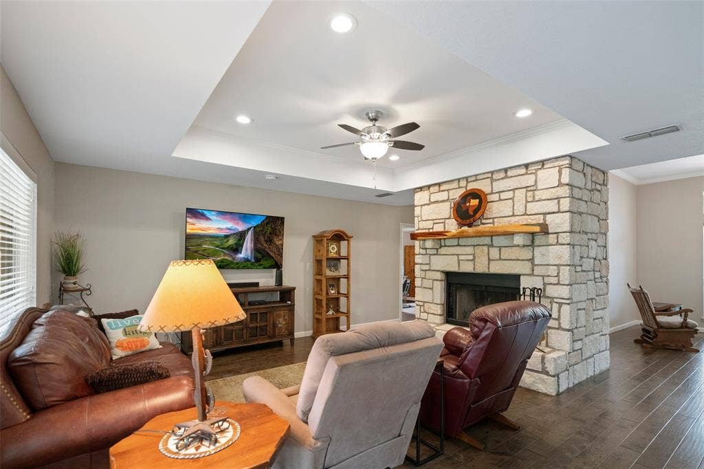 511 Casas Del Norte Court, Granbury, TX 76049 Tray ceiling featuring recessed lighting, expansive stone-clad fireplace, natural wood mantel, and dark wood-finish flooring