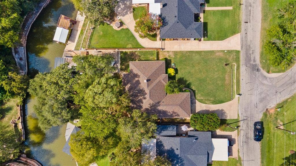 511 Casas Del Norte Court, Granbury, TX 76049 Aerial perspective featuring a waterfront property with a concrete driveway, multi-gabled shingle roof, mature trees, and boat dock
