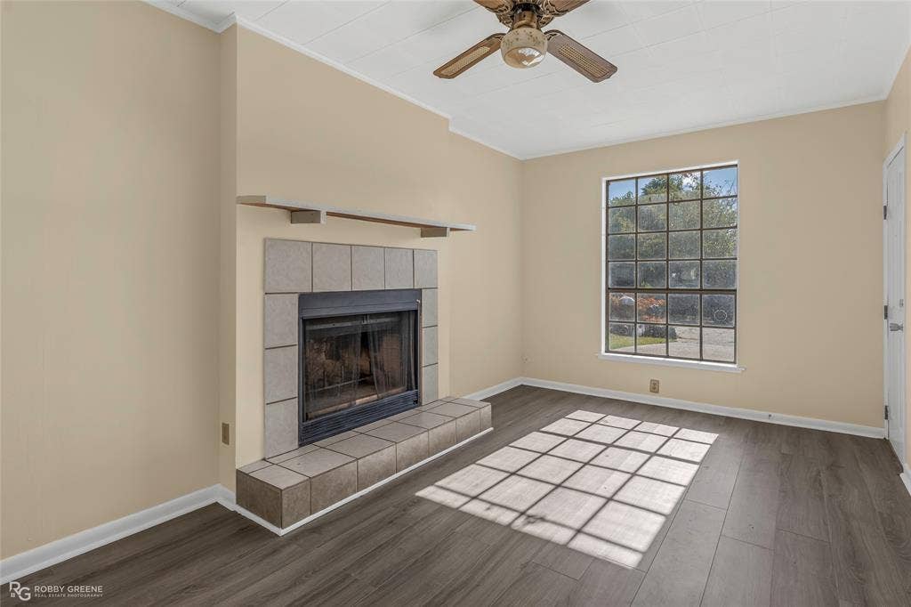 Fireplace with square tile surround and hearth, wood-finish flooring, grid-pattern window, and ceiling fan