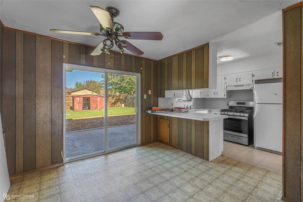 Kitchen featuring wood-paneled walls, sliding glass door, ceiling fan with light fixture, breakfast bar, and stainless steel range