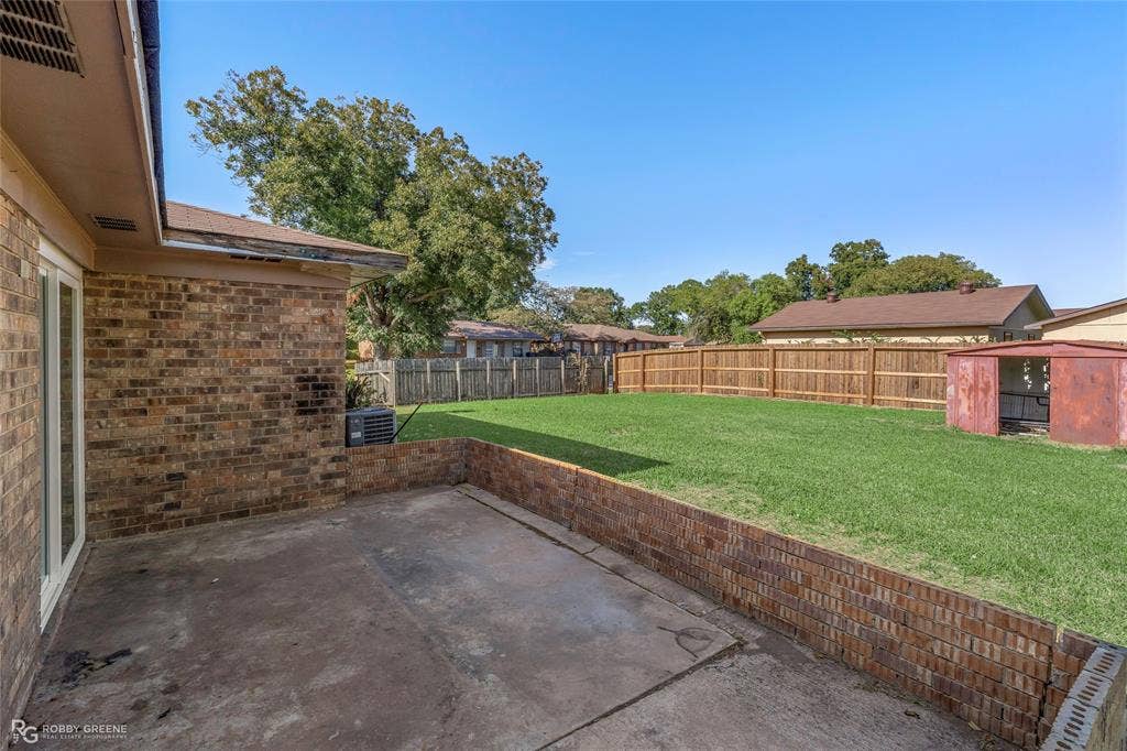 Rear exterior featuring a brick patio, a low brick retaining wall, a grass lawn, and wood privacy fencing