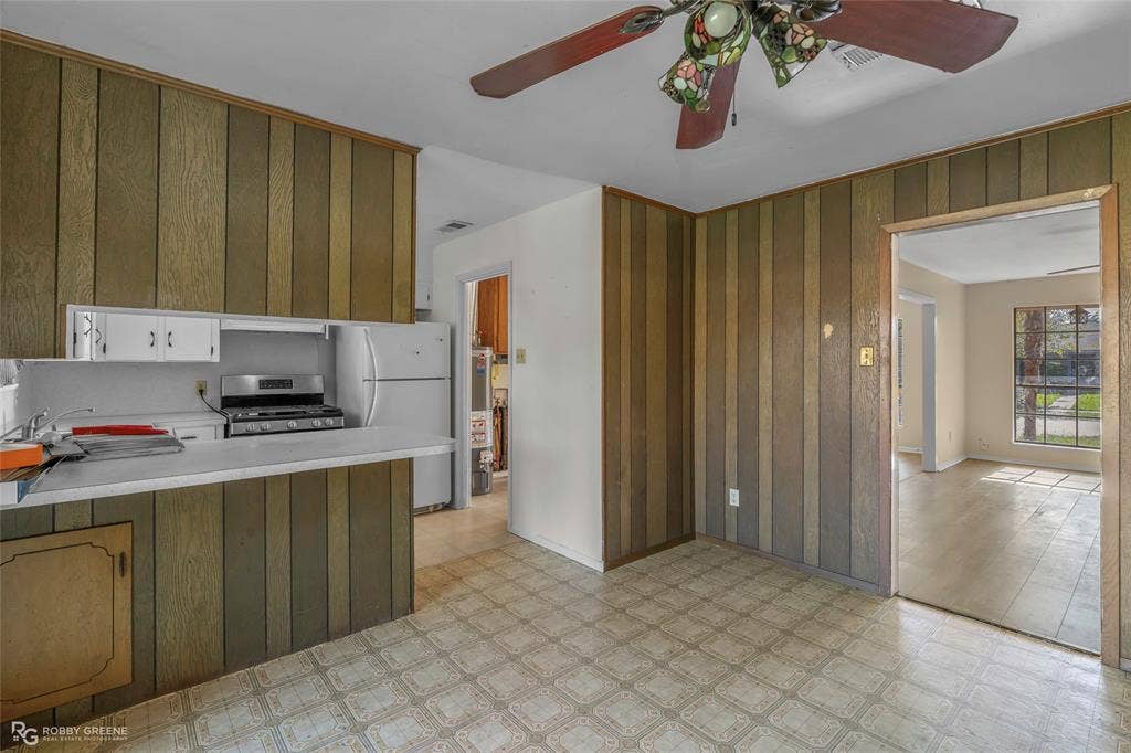Kitchen featuring wood-paneled wall treatments, a peninsula with a solid-surface countertop, and an attached multi-blade ceiling fan with decorative glass lighting