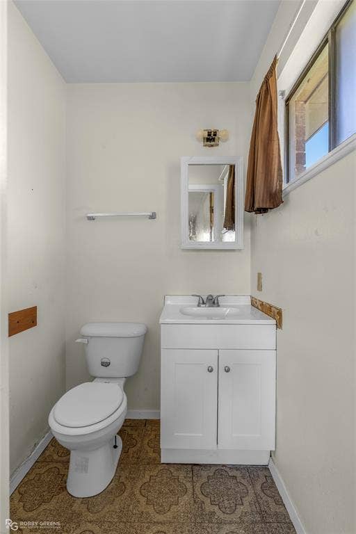 Bathroom featuring a white vanity cabinet with a integrated sink, polished metal faucet, white ceramic toilet, recessed medicine cabinet, and patterned tile flooring
