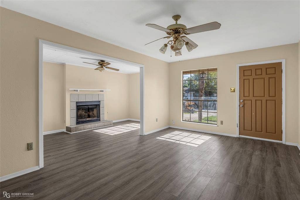 Wood-finish flooring, masonry fireplace with a mantel, grid-pattern window, ceiling fans, and a paneled entry door