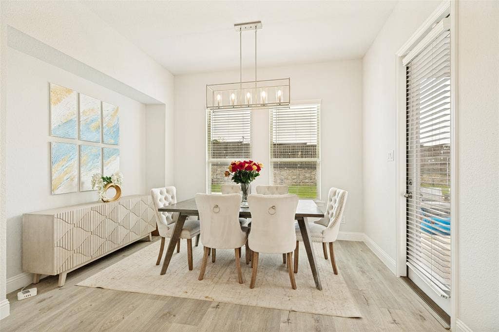 16931 Maple Bend Drive, Frisco, TX 75035 Dining area featuring wood-finish flooring, a rectangular linear pendant light fixture, dual windows, and an exterior door with integrated blinds