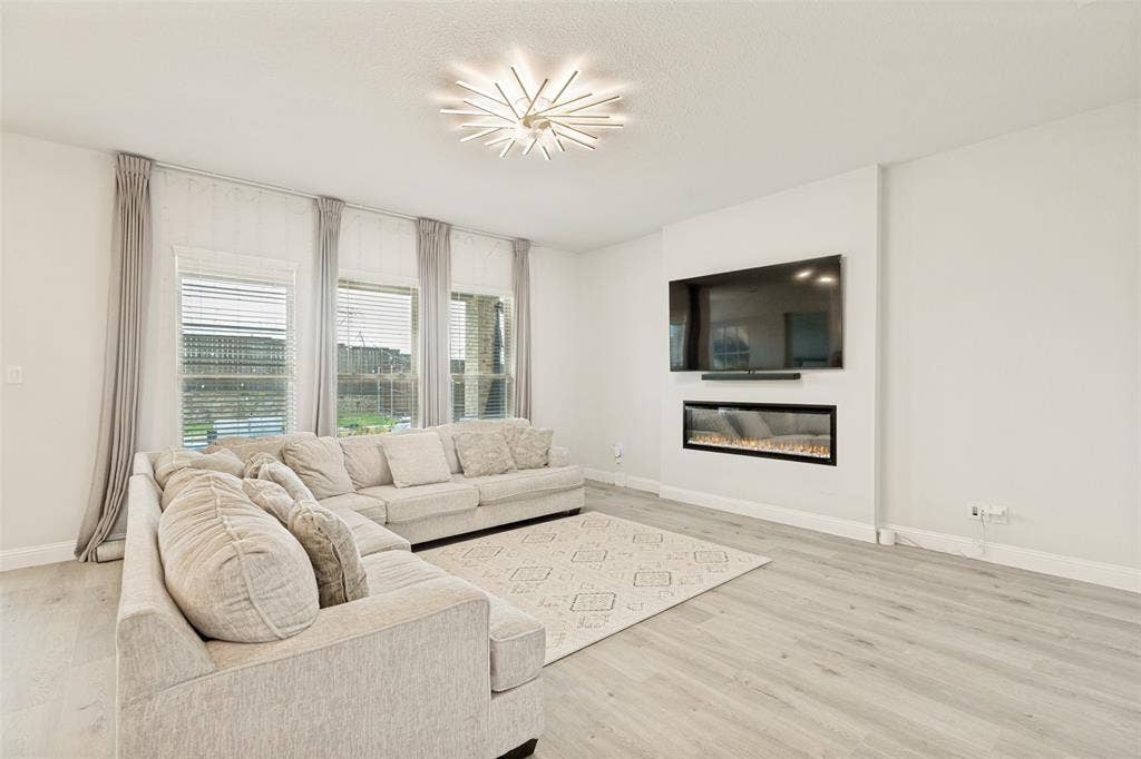 16931 Maple Bend Drive, Frisco, TX 75035 Living area featuring wood-finish flooring, a linear electric fireplace, and a contemporary starburst chandelier