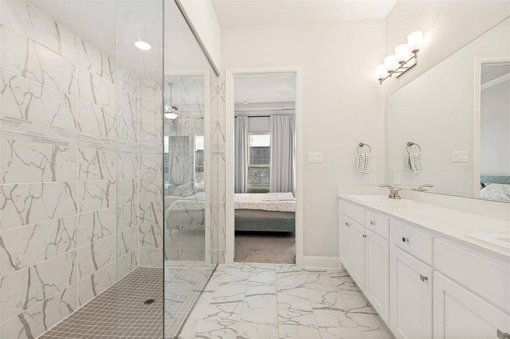 16931 Maple Bend Drive, Frisco, TX 75035 Bathroom featuring dual-sink vanity with white cabinetry, glass-enclosed walk-in shower with patterned tile surround, and tile flooring