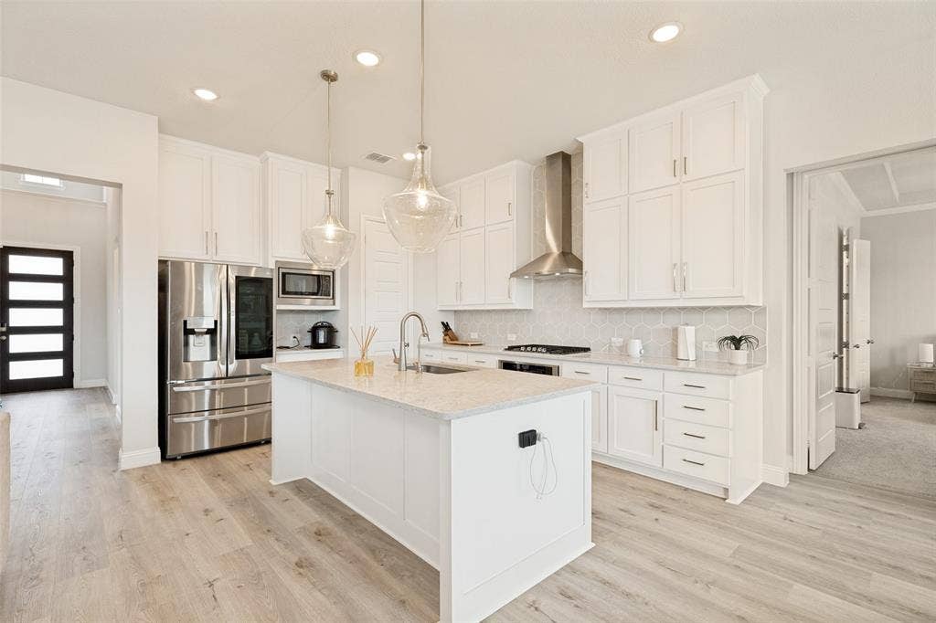 16931 Maple Bend Drive, Frisco, TX 75035 Kitchen featuring white cabinetry, an oversized central island with stone-finish countertops, stainless steel appliances, a modern chimney-style range hood, and wood-finish flooring
