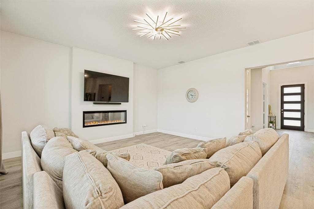 16931 Maple Bend Drive, Frisco, TX 75035 Linear recessed fireplace with stone surround, wood-finish flooring, starburst ceiling light fixture, and multipane front entry door