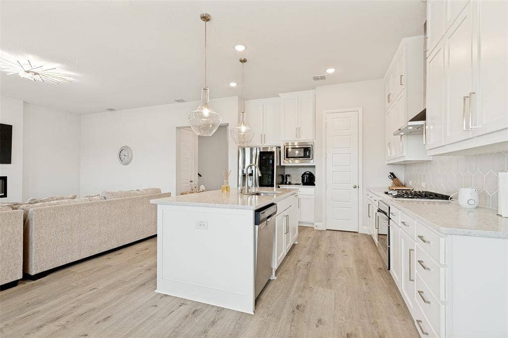 16931 Maple Bend Drive, Frisco, TX 75035 Kitchen featuring white shaker-style cabinetry, quartz countertops, a central island with a built-in stainless steel dishwasher, wood-finish flooring, and glass pendant lighting