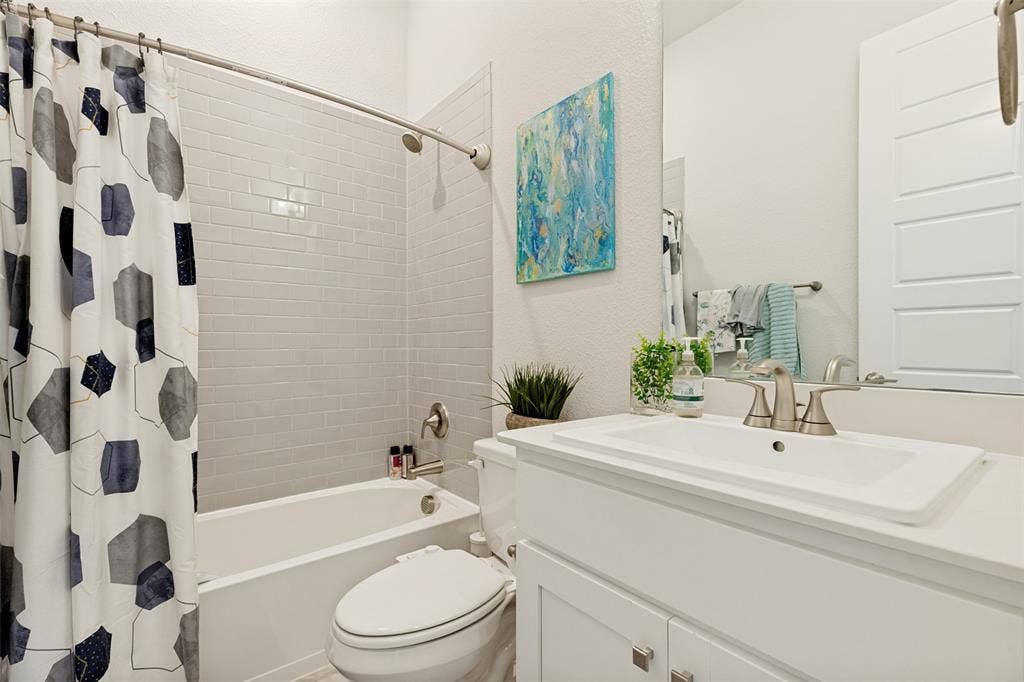 16931 Maple Bend Drive, Frisco, TX 75035 Bathroom featuring a white vanity with a rectangular sink, brushed nickel faucet, subway tile tub surround, and a large wall-mounted mirror