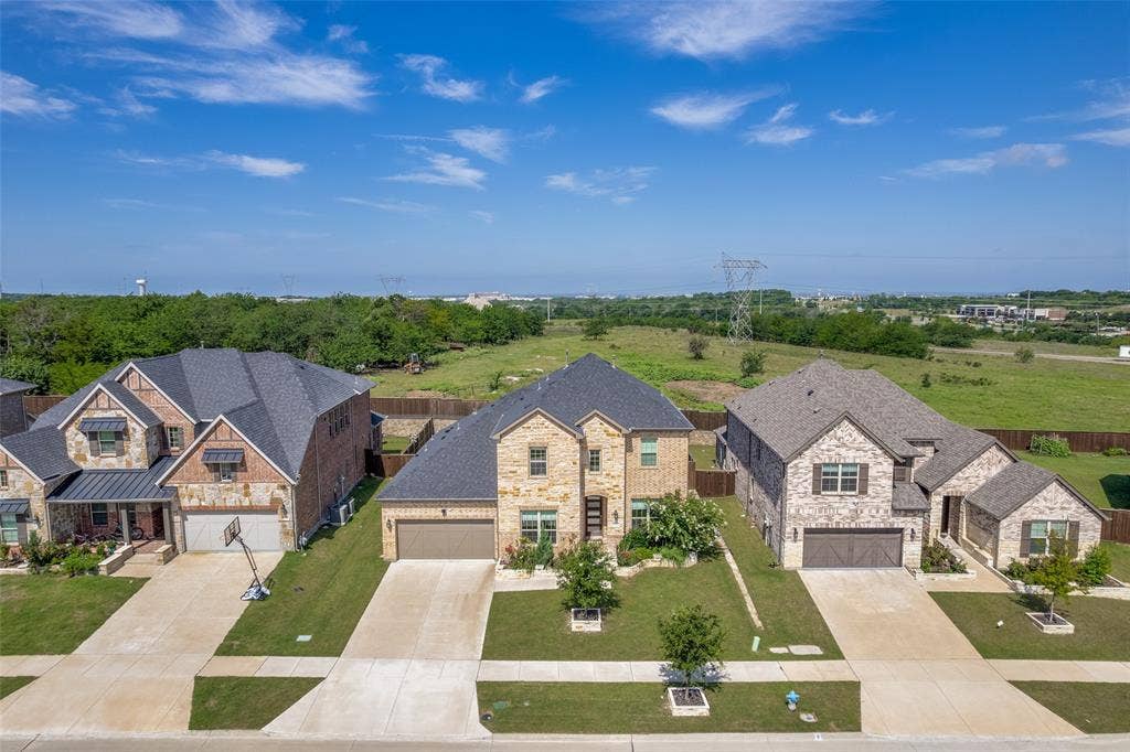 16931 Maple Bend Drive, Frisco, TX 75035 Multi-story exterior featuring a stone and brick facade, steeply pitched asphalt shingle roof, attached multi-car garage, concrete driveway, and professional landscaping