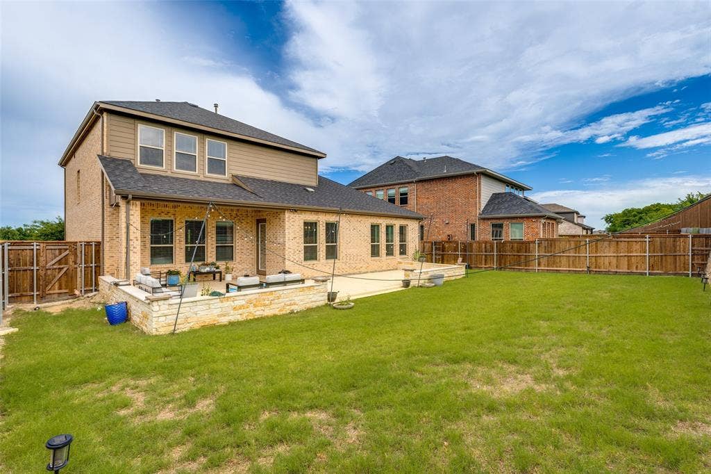 16931 Maple Bend Drive, Frisco, TX 75035 Two-story residence featuring a brick and siding exterior, expansive backyard with wood privacy fencing, and a raised stone-walled patio