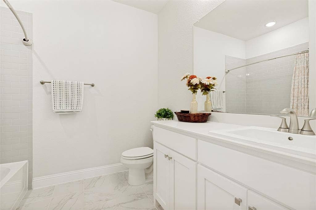 16931 Maple Bend Drive, Frisco, TX 75035 Bathroom featuring white shaker-style cabinetry, an integrated sink with polished metal fixtures, a large wall-mounted mirror, and tile flooring with a neutral pattern
