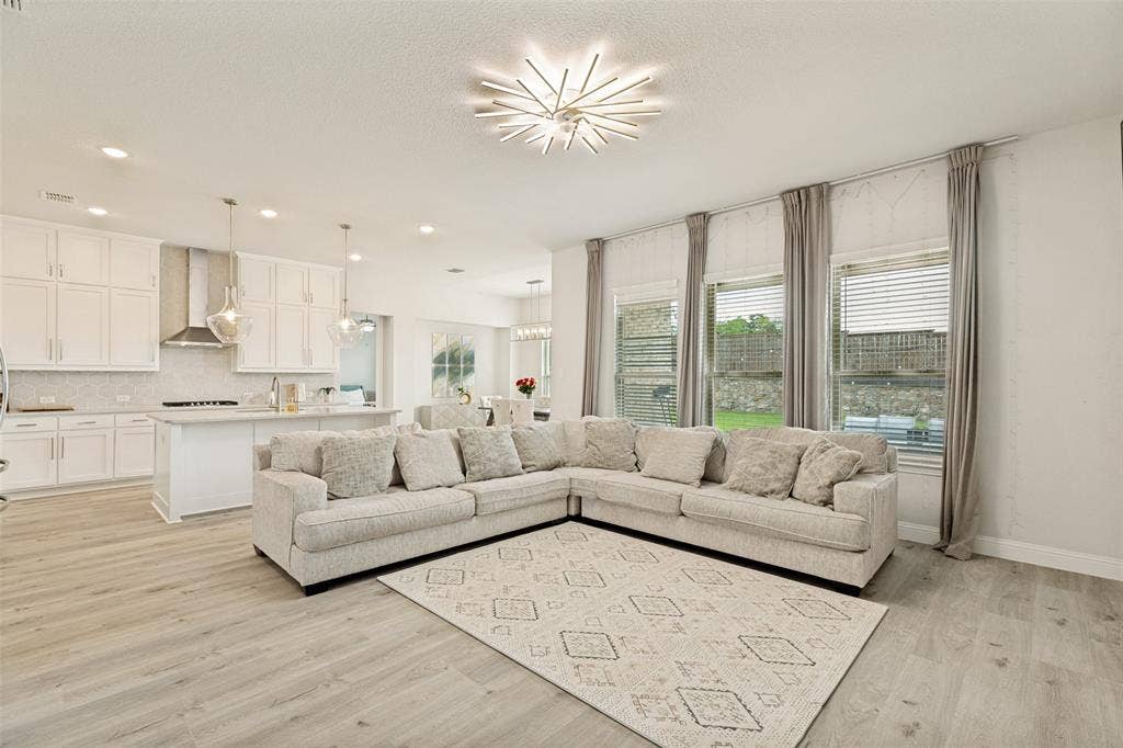 16931 Maple Bend Drive, Frisco, TX 75035 Open-concept kitchen featuring white cabinetry, a center island, and stainless steel appliances, complemented by wood-finish flooring and a multi-point sputnik-style chandelier
