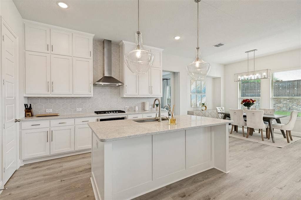 16931 Maple Bend Drive, Frisco, TX 75035 Kitchen featuring white cabinetry, quartz countertops, a stone hexagon-patterned backsplash, stainless steel chimney-style range hood, and wood-finish flooring