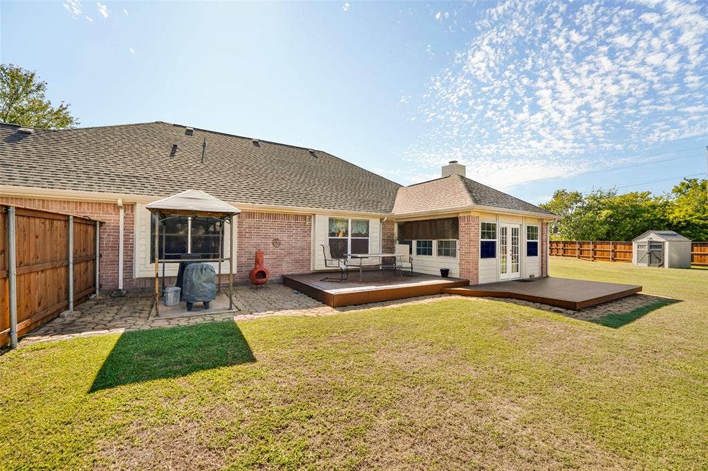 8700 Broken Bow Drive, Greenville, TX 75402 Sunroom opens up to a multi-level TREX deck, paved patio area with BBQ canopy, wood fencing, and a detached storage shed.