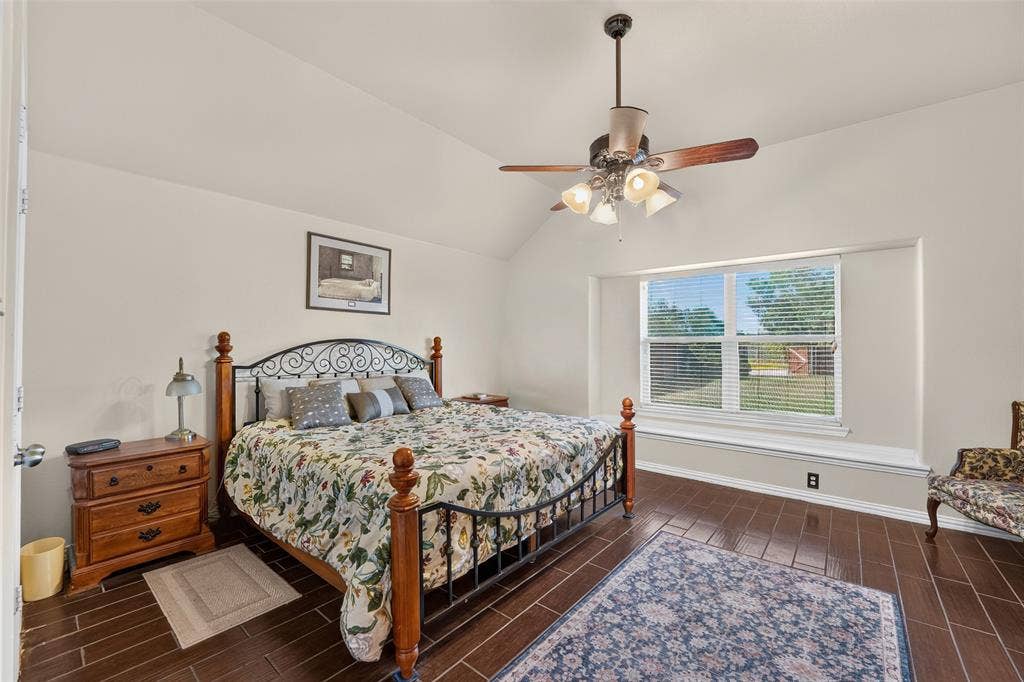 8700 Broken Bow Drive, Greenville, TX 75402 Spacious primary bedroom featuring vaulted ceilings with fan, abundant natural light, and a cozy window seat overlooking the backyard.