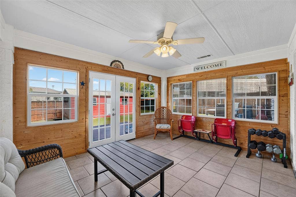 8700 Broken Bow Drive, Greenville, TX 75402 Temperature-controlled sunroom featuring abundant natural light, wood-plank walls, tile flooring, ceiling fan, and French doors leading to the backyard.
