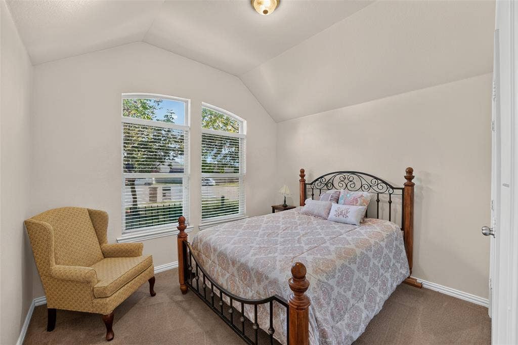8700 Broken Bow Drive, Greenville, TX 75402 Sec. bedroom in front of home with a vaulted ceiling featuring a central flush-mount light fixture and dual arched windows with blinds.