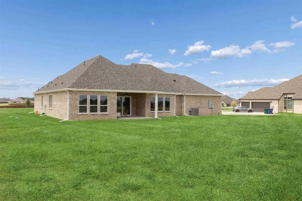 151 Quiet Waters Way, Waxahachie, TX 75165 Brick exterior residence featuring an expansive lawn, a covered rear patio, and a multi-car garage