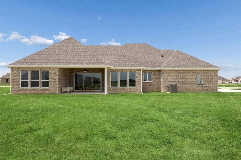151 Quiet Waters Way, Waxahachie, TX 75165 Brick exterior featuring a covered patio, shingle roof, expansive lawn, and sliding glass doors