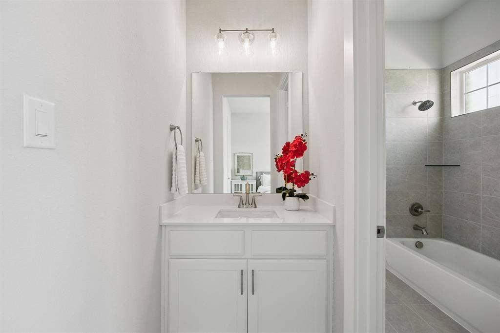 151 Quiet Waters Way, Waxahachie, TX 75165 Bathroom featuring white shaker-style cabinetry, a rectangular vanity sink with a polished chrome faucet, a frameless vanity mirror, a three-light fixture, and a tub-shower combination with light-toned ceramic tile surround