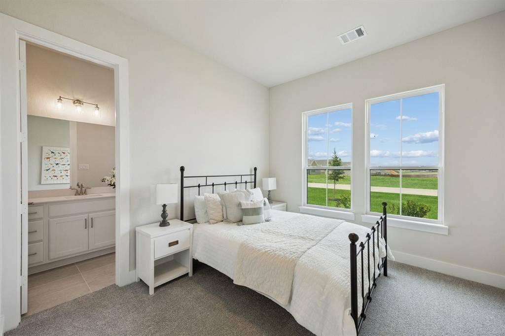 151 Quiet Waters Way, Waxahachie, TX 75165 Neutral-toned bedroom featuring wall-to-wall carpeting, two oversized windows, and a bathroom equipped with a vanity featuring a light-toned countertop