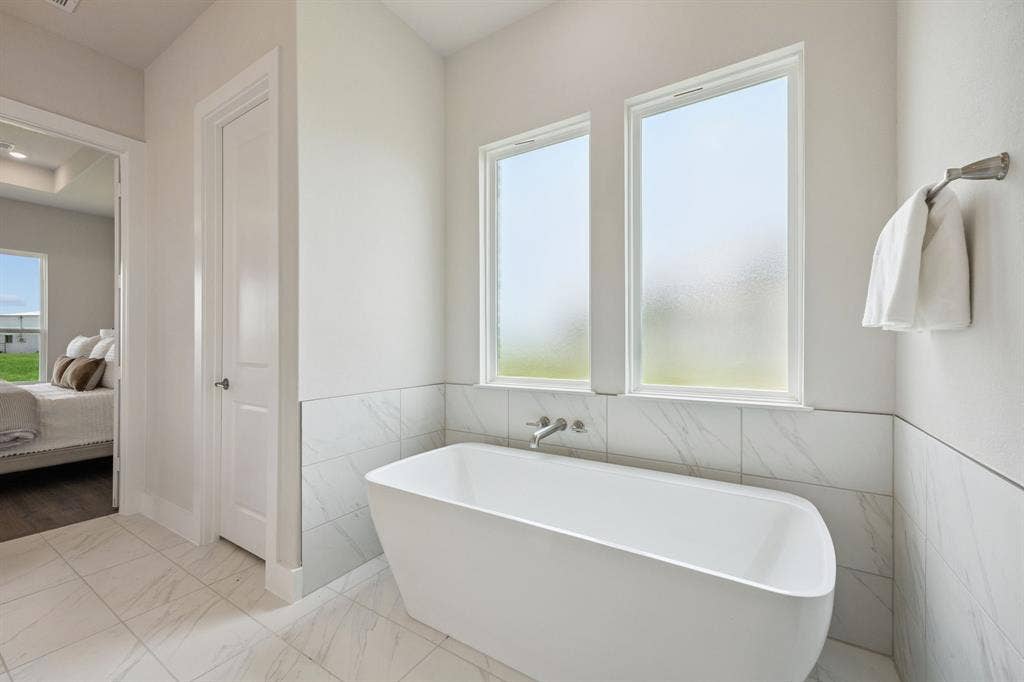 151 Quiet Waters Way, Waxahachie, TX 75165 Freestanding soaking tub with a wall-mounted faucet, dual windows with frosted glass, and large-format tile surround