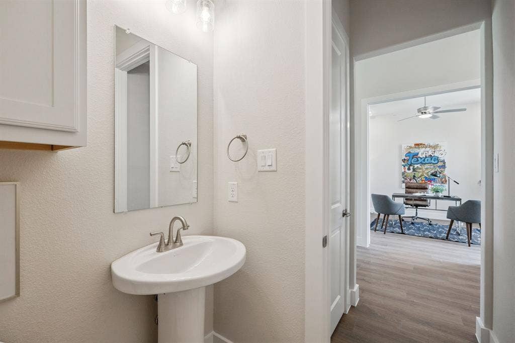 151 Quiet Waters Way, Waxahachie, TX 75165 White pedestal sink featuring a polished nickel faucet, wall-mounted rectangular mirror, and overhead decorative lighting fixture