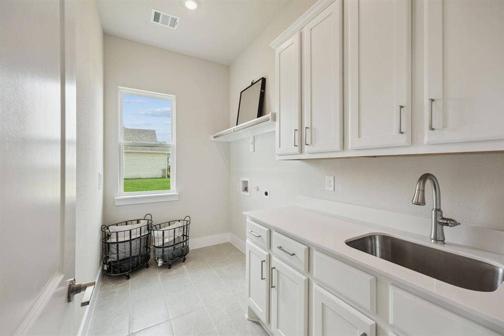 151 Quiet Waters Way, Waxahachie, TX 75165 Utility space featuring white shaker-style cabinetry, a light-toned solid surface countertop, an undermount stainless steel sink with a high-arc faucet, and light-toned ceramic tile flooring